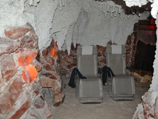 sitzplaetze-salzgrotte Eine Salzgrotte mit zwei Liegestühlen, umgeben von salzbedeckten Wänden und gedämpfter Beleuchtung.