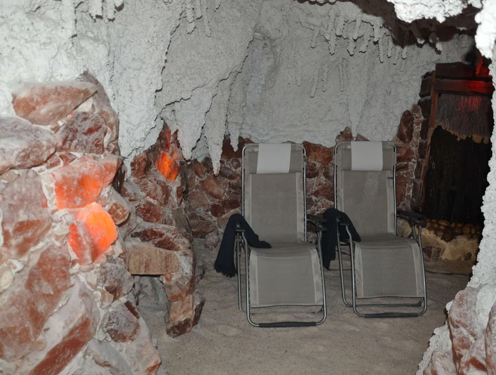 sitzplaetze-salzgrotte Eine Salzgrotte mit zwei Liegestühlen, umgeben von salzbedeckten Wänden und gedämpfter Beleuchtung.