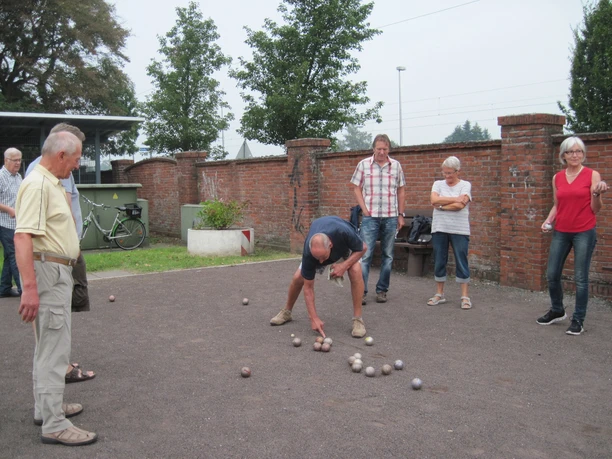 Donnerstag-Gruppe Eine Gruppe von Menschen spielt Boule auf einem Kiesplatz vor einer alten Backsteinmauer.