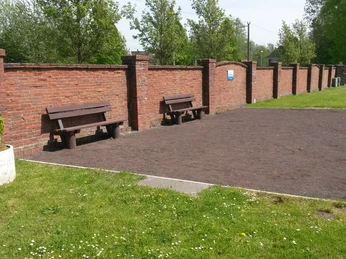 Bouleplatz Augustfehn Ein gepflegter Bouleplatz mit Kies, begrenzt von einer roten Ziegelmauer und umgeben von grünen Bäumen.