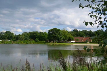 An idyllic campsite lies in front of a gently undulating body of water, surrounded by lush greenery.
