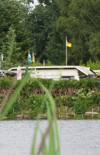 Mobilheime am Campingplatz Mobilheime an einem idyllischen Campingplatz, umgeben von grünen Bäumen und Wasser, Fahnen wehen im Wind.