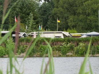 Mobilheime am Campingplatz Mobilheime an einem idyllischen Campingplatz, umgeben von grünen Bäumen und Wasser, Fahnen wehen im Wind.