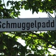 Wegweiser Schmuggelpadd Ein Straßenschild mit dem Namen "Schmuggelpadd", umgeben von grünen Kastanienblättern.