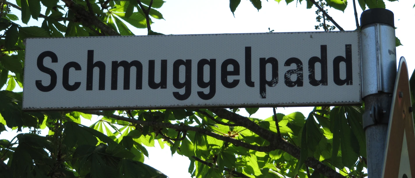 Wegweiser Schmuggelpadd Ein Straßenschild mit dem Namen "Schmuggelpadd", umgeben von grünen Kastanienblättern.