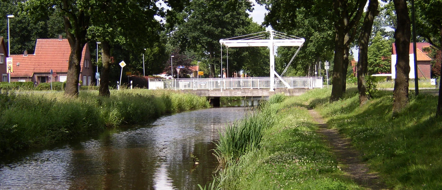 Augustfehn Kanal mit Treidelpfad Ein idyllischer Kanal fließt unter einer modernen Fußgängerbrücke, begleitet von einem erholsamen Treidelpfad und gesäumt von Bäumen. Der Augustfehn Kanal bietet eine malerische Kulisse für Spaziergänger und Naturliebhaber.