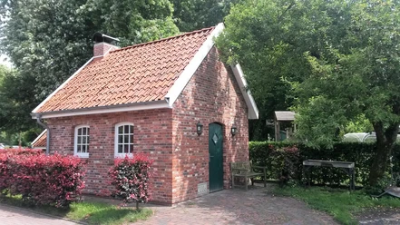 Backhaus an der Hengstforder Mühle Ein Backhaus aus rotem Ziegelstein mit Satteldach, umgeben von grünen Bäumen und roten Sträuchern.
