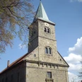 Petruskirche Steinhude Steinernes Kirchenschiff mit Kirchturm, schiefer Spitze und Uhr unter blauem Himmel mit Wolken.