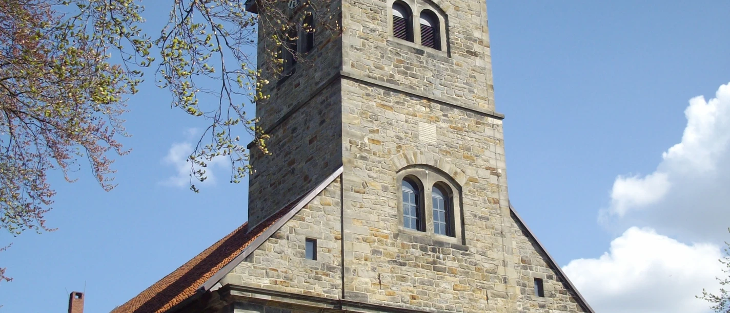 Petruskirche Steinhude Steinernes Kirchenschiff mit Kirchturm, schiefer Spitze und Uhr unter blauem Himmel mit Wolken.