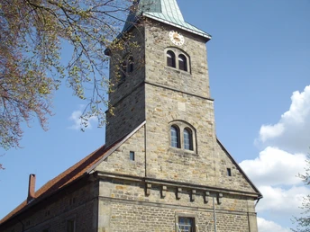 Petruskirche Steinhude Steinernes Kirchenschiff mit Kirchturm, schiefer Spitze und Uhr unter blauem Himmel mit Wolken.
