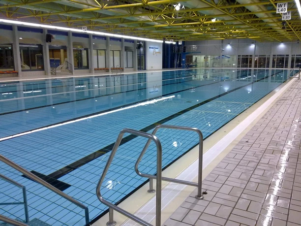 Wunstorf Elements Ein modernes Hallenbad mit verglasten Wänden und einem großen Schwimmbecken, das klar blau schimmert.