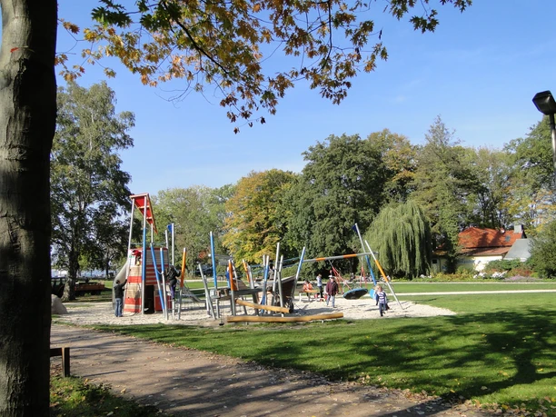 Ein weitläufiger Spielplatz mit modernen Kletteranlagen, umgeben von Bäumen im Park.