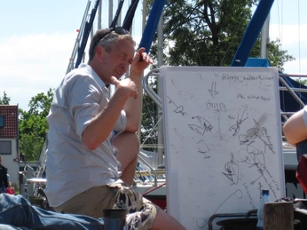 Segelunterricht mit Holger Stintat Holger Stintat zeigt Segelschülern theoretische Grundlagen auf einer Tafel im Freien.