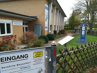 Im Vordergrund ist der Eingang des Wasser + mehr Erlebnisparks in Hohenholz zu sehen. Ein Schild informiert über den Zugang.