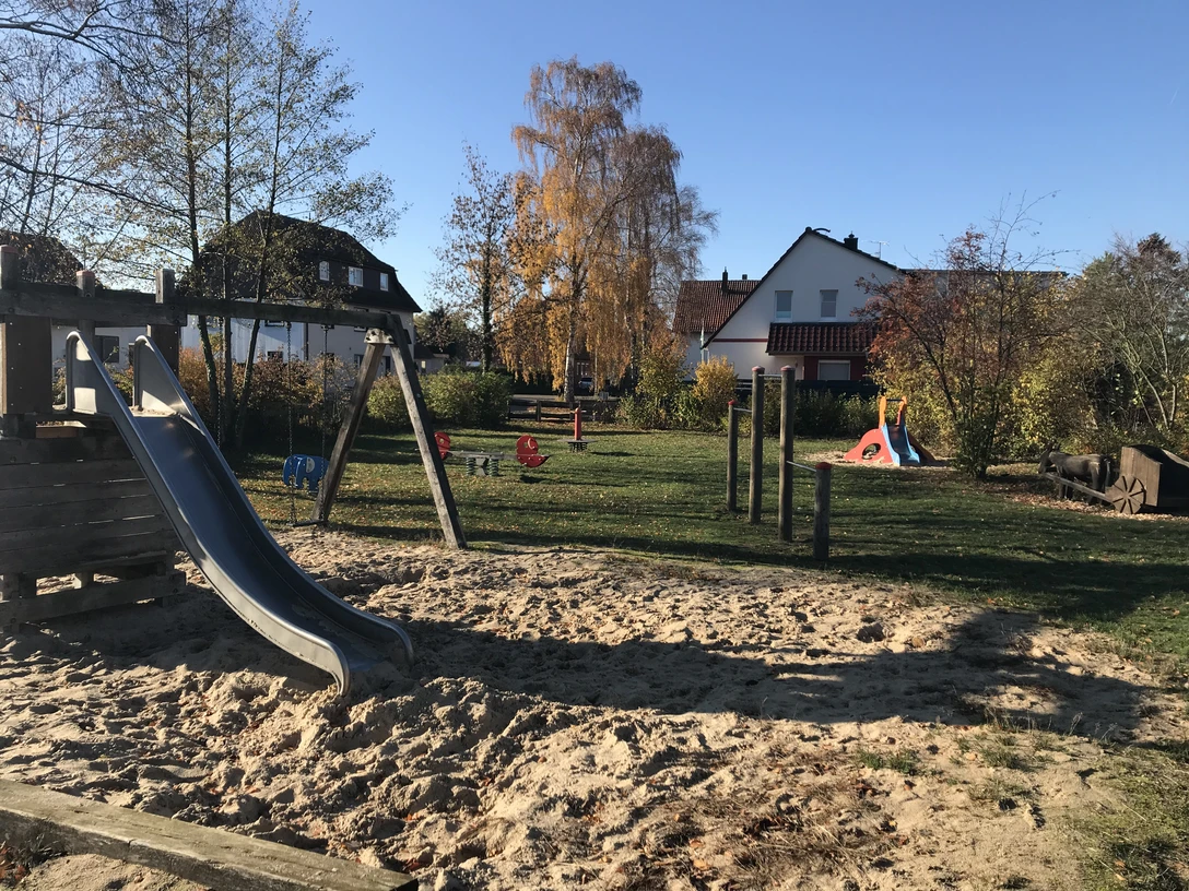 Spielplatz Masurenplatz Ein moderner Spielplatz mit Klettergerüst, Rutsche und Wippe, eingerahmt von herbstlichen Bäumen.
