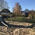 Spielplatz Masurenplatz Ein moderner Spielplatz mit Klettergerüst, Rutsche und Wippe, eingerahmt von herbstlichen Bäumen.