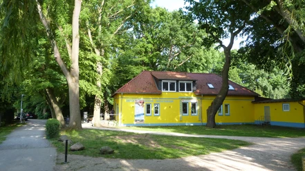 A yellow building with a red roof and several windows, nestled in a green park.