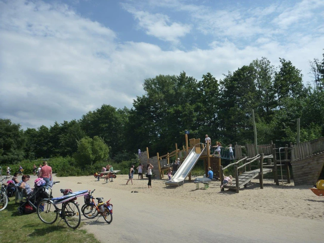 Spielplatz Badeinsel Ein lebendiger Spielplatz mit Holzkonstruktionen, Rutsche und Kindern beim Spielen im sonnigen Park.