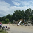 Spielplatz Badeinsel Ein lebendiger Spielplatz mit Holzkonstruktionen, Rutsche und Kindern beim Spielen im sonnigen Park.