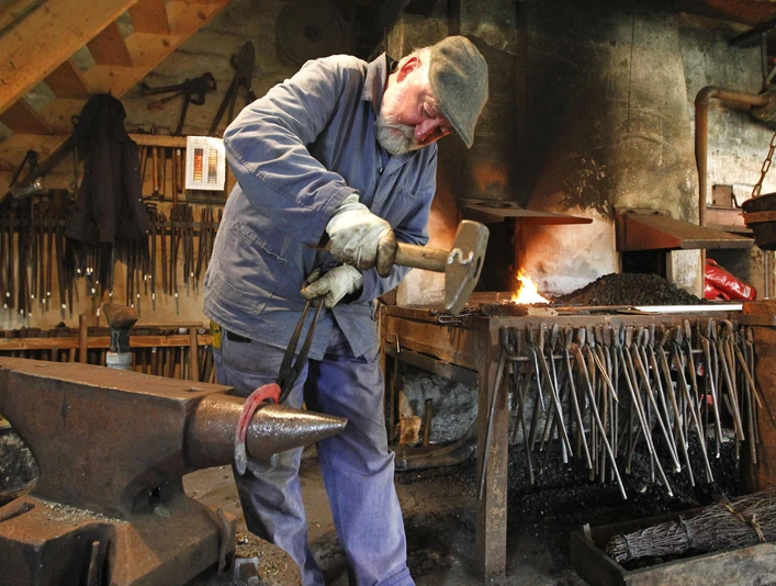 Ein Hufschmied schlägt in einer authentischen Werkstatt in Helstorf gekonnt auf ein Eisenstück am Amboss.