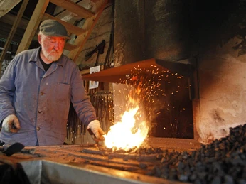 Ein Hufschmied bearbeitet glühendes Eisen in einer traditionell eingerichteten Werkstatt.