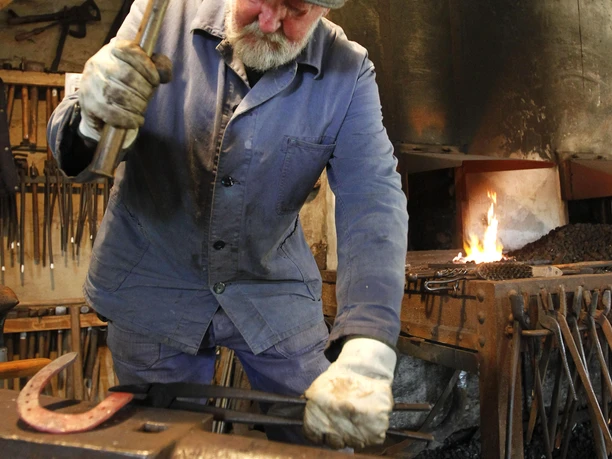 Hufschmiedemuseum Helstorf Ein Hufschmied arbeitet konzentriert an einem Amboss in einer traditionellen Schmiede.