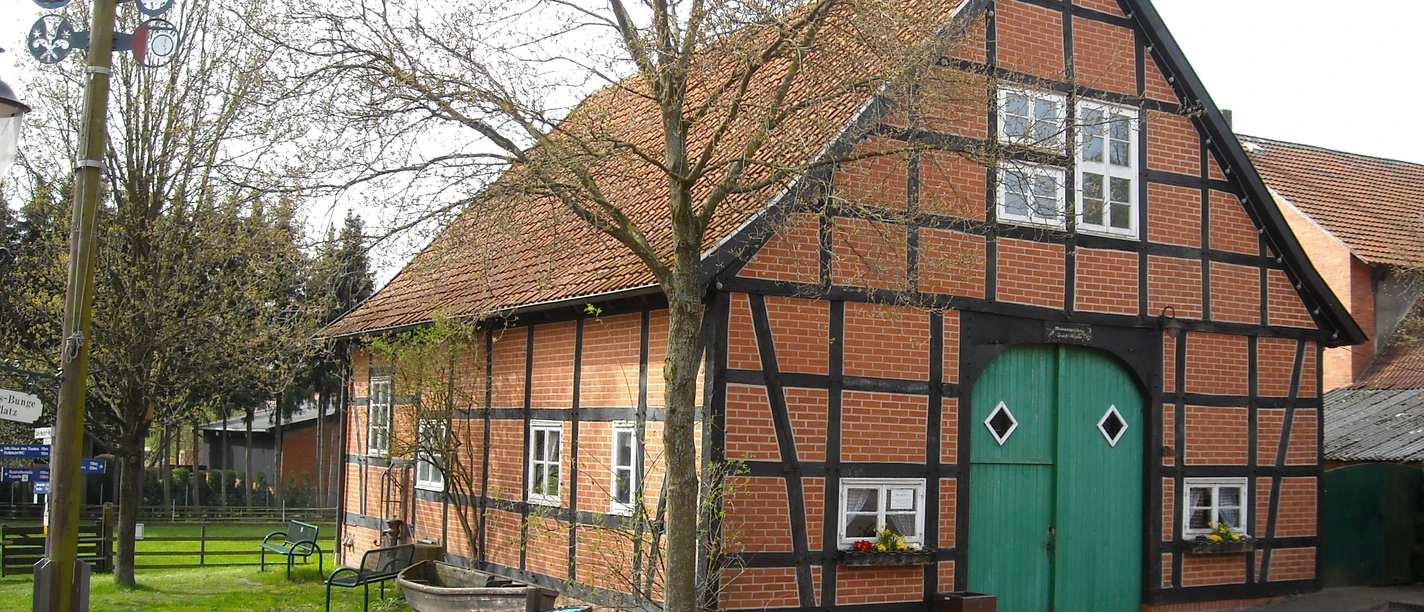Museum Mardorf Fachwerkhof im Grünen, mit rotem Backstein und blauem Tor; umgeben von Bäumen und Bänken.