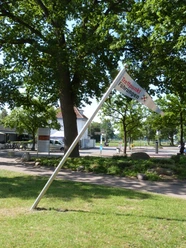 Treffpunkf für Gästeführungen Eine Fahne mit der Aufschrift "Treffpunkt Führungen" neigt sich neben einem Weg in einem grünen Parkbereich.