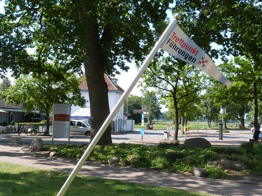 Treffpunkf für Gästeführungen Eine Fahne mit der Aufschrift "Treffpunkt Führungen" neigt sich neben einem Weg in einem grünen Parkbereich.A flag with the inscription "Treffpunkt Führungen" (meeting point for guided tours) leans next to a path in a green park area.Et flag med påskriften "Treffpunkt Führungen" (mødested for guidede ture) står ved siden af en sti i et grønt parkområde.Een vlag met het opschrift "Treffpunkt Führungen" (trefpunt voor rondleidingen) hangt naast een pad in een groen parkgebied.