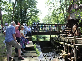 Wassermühle Laderholz mit Besuchern Besucher genießen die Szenerie vor der historischen Wassermühle Laderholz bei sonnigem Wetter.