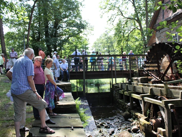 Wassermühle Laderholz mit Besuchern Besucher genießen die Szenerie vor der historischen Wassermühle Laderholz bei sonnigem Wetter.