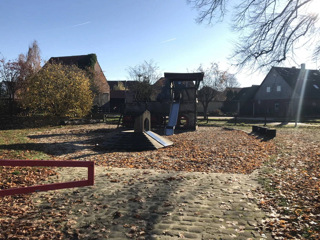 Spielplatz mit Rutsche und Klettergerüst, umgeben von Herbstlaub und ruhigen Wohnhäusern.