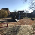 Spielplatz mit Rutsche und Klettergerüst, umgeben von Herbstlaub und ruhigen Wohnhäusern.