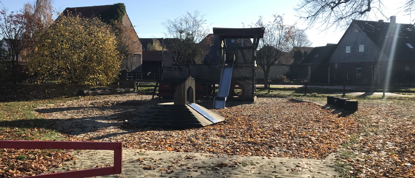 Spielplatz mit Rutsche und Klettergerüst, umgeben von Herbstlaub und ruhigen Wohnhäusern.
