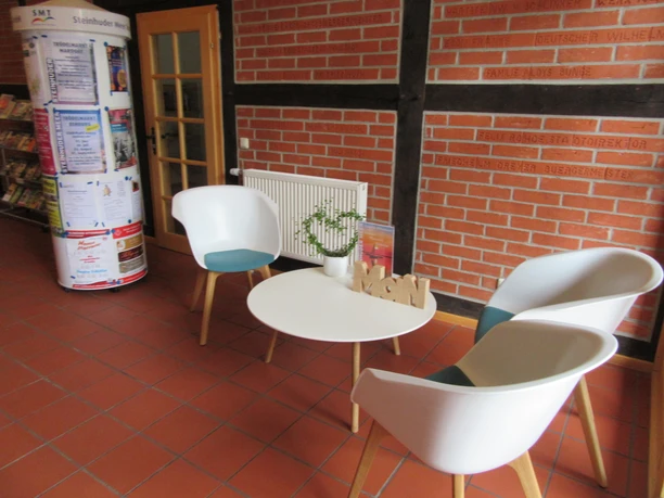 Bright, modern seating area with white armchairs and table on a red tiled floor in a public space.