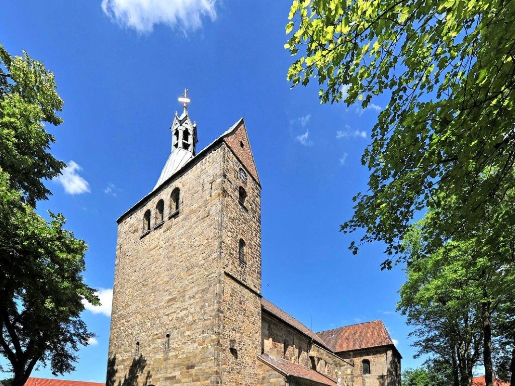 Stiftskirche in Wunstorf Stiftskirche Wunstorf, romanischer Baustil, charakteristischer Turm aus Sandstein, umgeben von Bäumen.