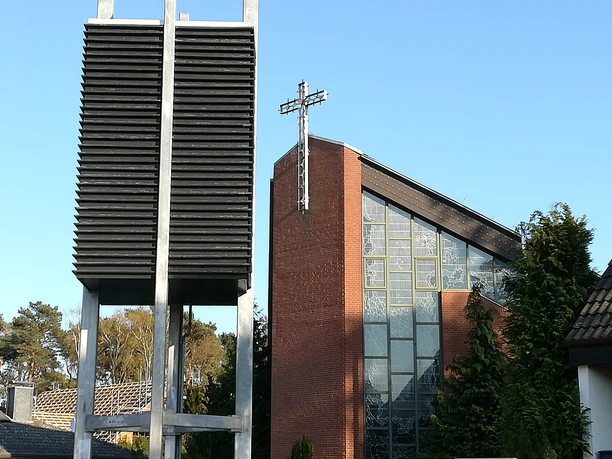 Blick auf die St. Hedwig Kirche Steinhude Backstein-Kirche unter blauem Himmel, markantes Glockenspiel aus silberfarbenen Lamellen im Vordergrund.
