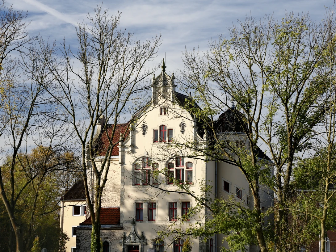Ein historisches Gebäude mit verzierten Fenstern und Turmspitze, umrahmt von Bäumen im Herbst.