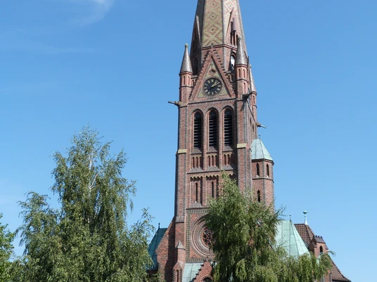 Kirche Hagenburg Front Backsteinkirche mit hohem, verzierten Turm und Uhr, umrahmt von Bäumen unter klarem Himmel.