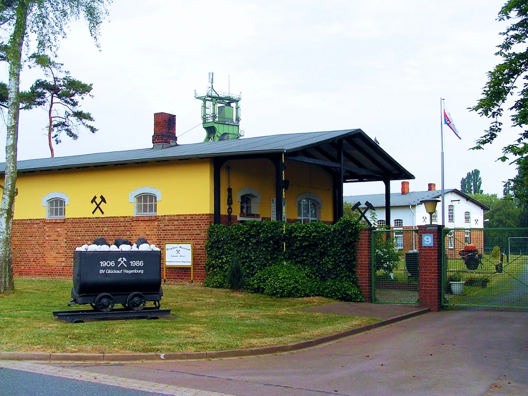 Das Bergbaumuseum Altenhagen zeigt ein gelbes Gebäude mit Förderturm und alten Förderwagen, umgeben von Bäumen.