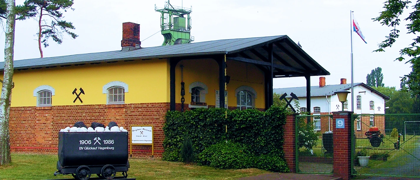 Bergbaumuseum Altenhagen Das Bergbaumuseum Altenhagen zeigt ein gelbes Gebäude mit Förderturm und alten Förderwagen, umgeben von Bäumen.