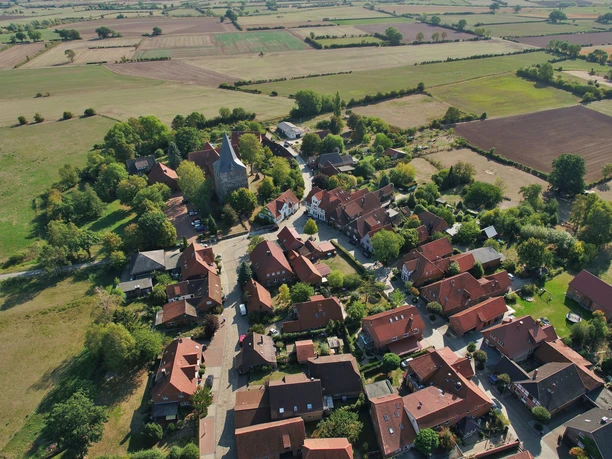 mandelsloh-st.osdag-kirche-luftbild Luftaufnahme von Mandelsloh, zeigt die St. Osdag-Kirche umgeben von rotgedeckten Häusern und Feldern.