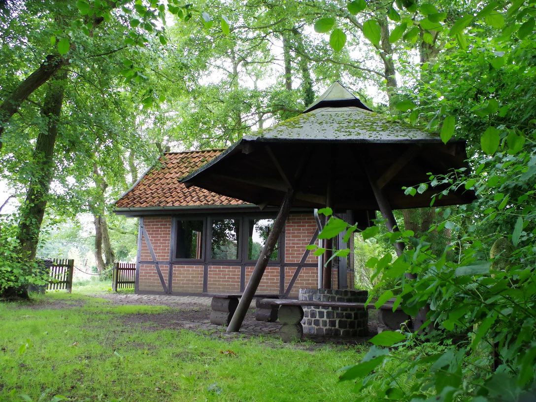 Grillhütte Dudensen Grillhütte Dudensen aus roten Ziegeln mit Walmdach, umgeben von dichtem Laubwald und grünem Rasen.