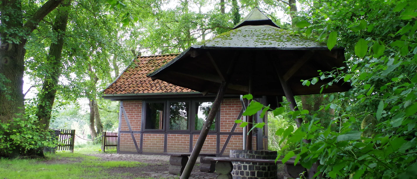 Grillhütte Dudensen Grillhütte Dudensen aus roten Ziegeln mit Walmdach, umgeben von dichtem Laubwald und grünem Rasen.