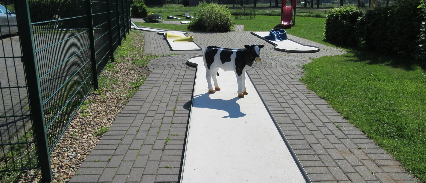 A sunlit mini-golf course with a deceptive toy dog, surrounded by green vegetation.
