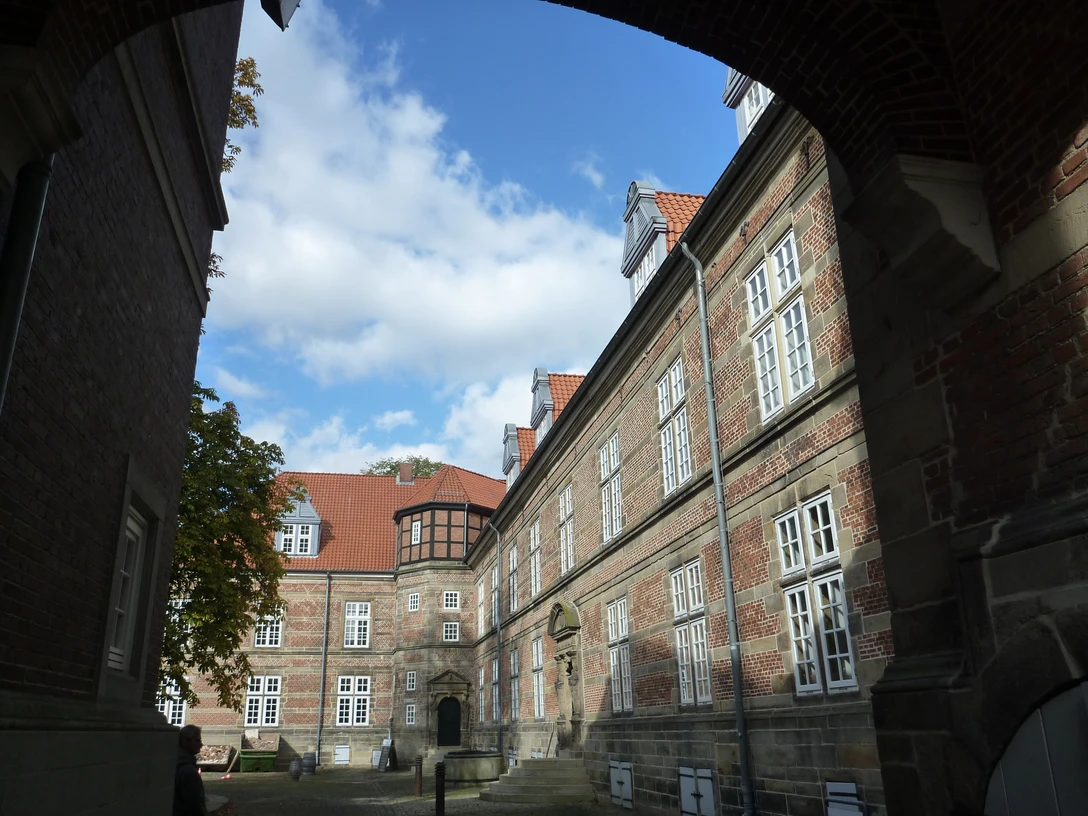 Im Innenhof des Schlosses Landestrost bieten historische Backsteinfassaden und rote Dachziegeln eine beeindruckende Kulisse unter einem blauen Himmel mit weißen Wolken.