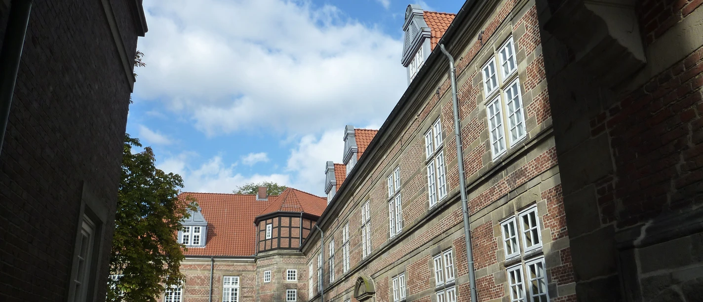 Im Innenhof des Schlosses Landestrost bieten historische Backsteinfassaden und rote Dachziegeln eine beeindruckende Kulisse unter einem blauen Himmel mit weißen Wolken.