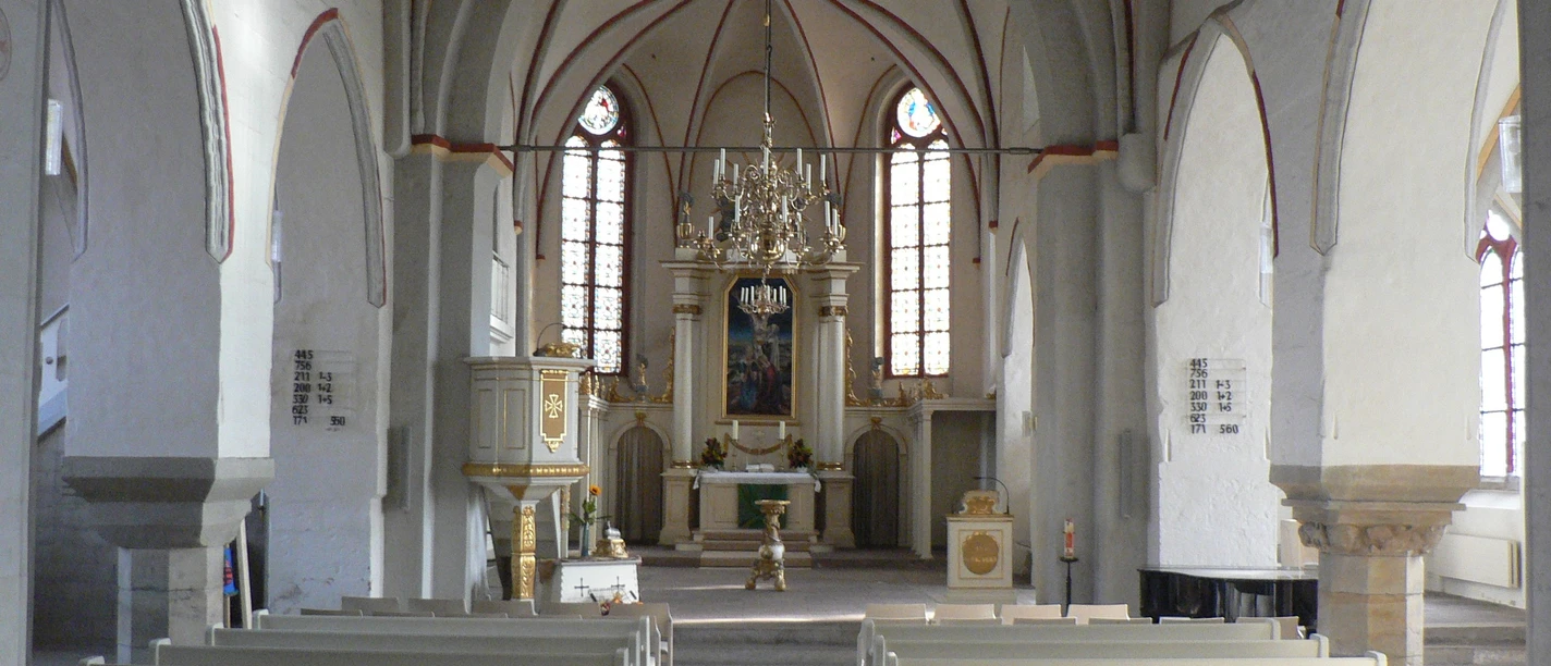 Altar Liebfrauenkirche Blick in eine helle Kirche mit weißem Gewölbe, hölzernen Bänken und kunstvollem Altarbild.