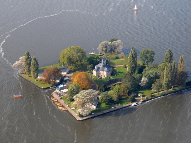 Luftbild Inselfestung Wilhelmstein Insel mit Festungsanlagen, umgeben von Wasser, gesäumt von Bäumen und abfahrenden Segelbooten.