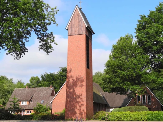 Friedenskirche Augustfehn Die Friedenskirche Augustfehn ist ein eindrucksvoller roter Backsteinturm, umgeben von grünen Büschen und Bäumen.